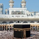 Thousands of pilgrims gather for prayer around the Kaaba in Mecca, Saudi Arabia during daylight.