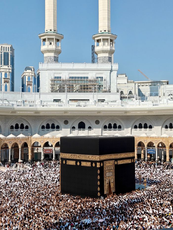 Thousands of pilgrims gather for prayer around the Kaaba in Mecca, Saudi Arabia during daylight.
